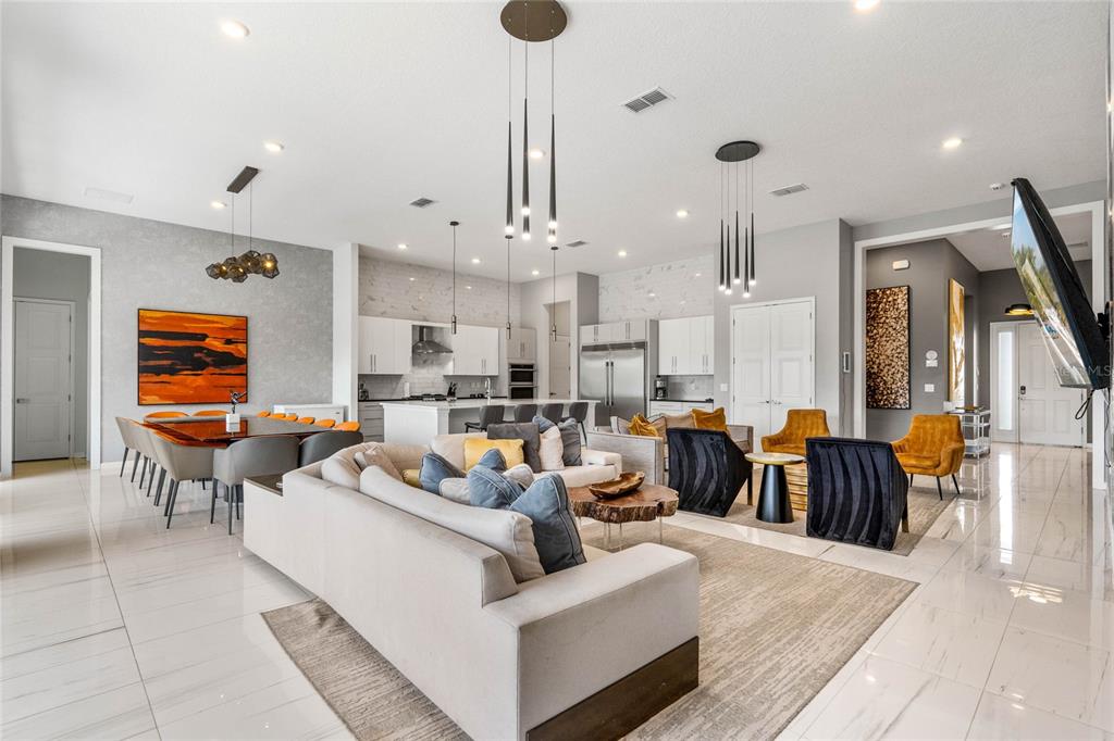 An open-concept living and dining area features white tile floors, modern lighting, and neutral furniture — 1743 OAK BLOSSOM DRIVE, DAVENPORT, FL