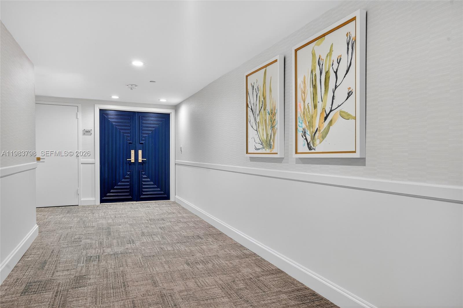 A hallway features a blue double door, two framed botanical prints, and patterned carpeting — 19670 Beach Rd # A601, Tequesta FL 33469, TEQUESTA, FL