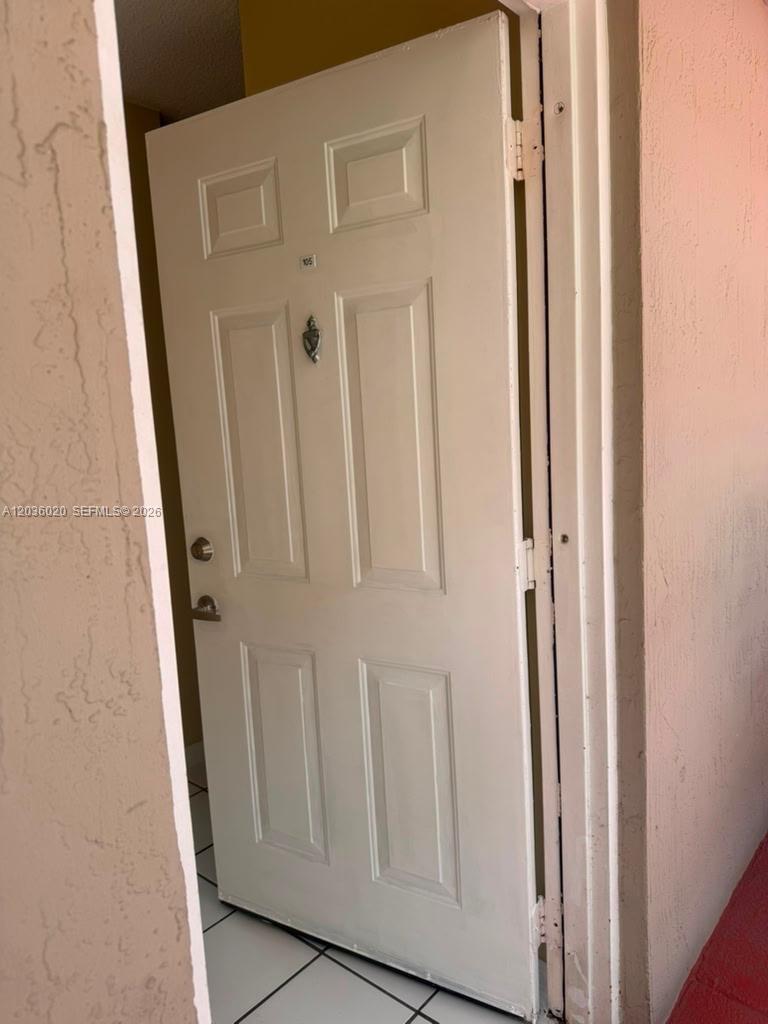 A white, six-panel entry door with a silver knocker and handle is set in a wall — 600 NW 32nd Pl # 105, Miami FL 33125, MIAMI, FL