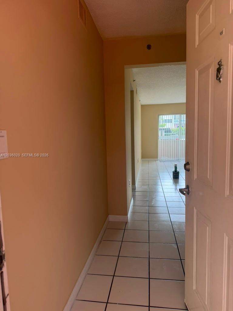 An entryway with white tiled floors leads into a hallway toward a sliding glass door — 600 NW 32nd Pl # 105, Miami FL 33125, MIAMI, FL