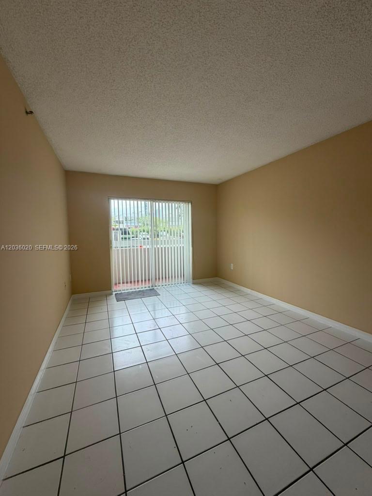 An empty room features beige walls, white tile flooring, and a sliding glass balcony door — 600 NW 32nd Pl # 105, Miami FL 33125, MIAMI, FL