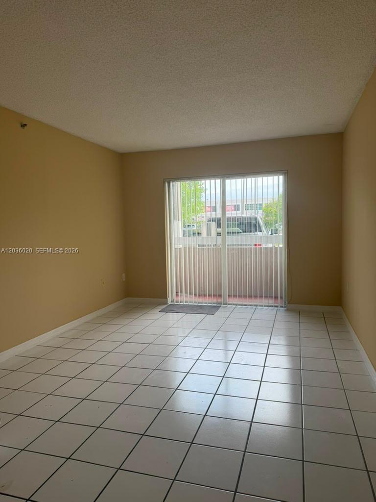 An empty room with beige walls, white tile flooring, and a sliding glass door — 600 NW 32nd Pl # 105, Miami FL 33125, MIAMI, FL