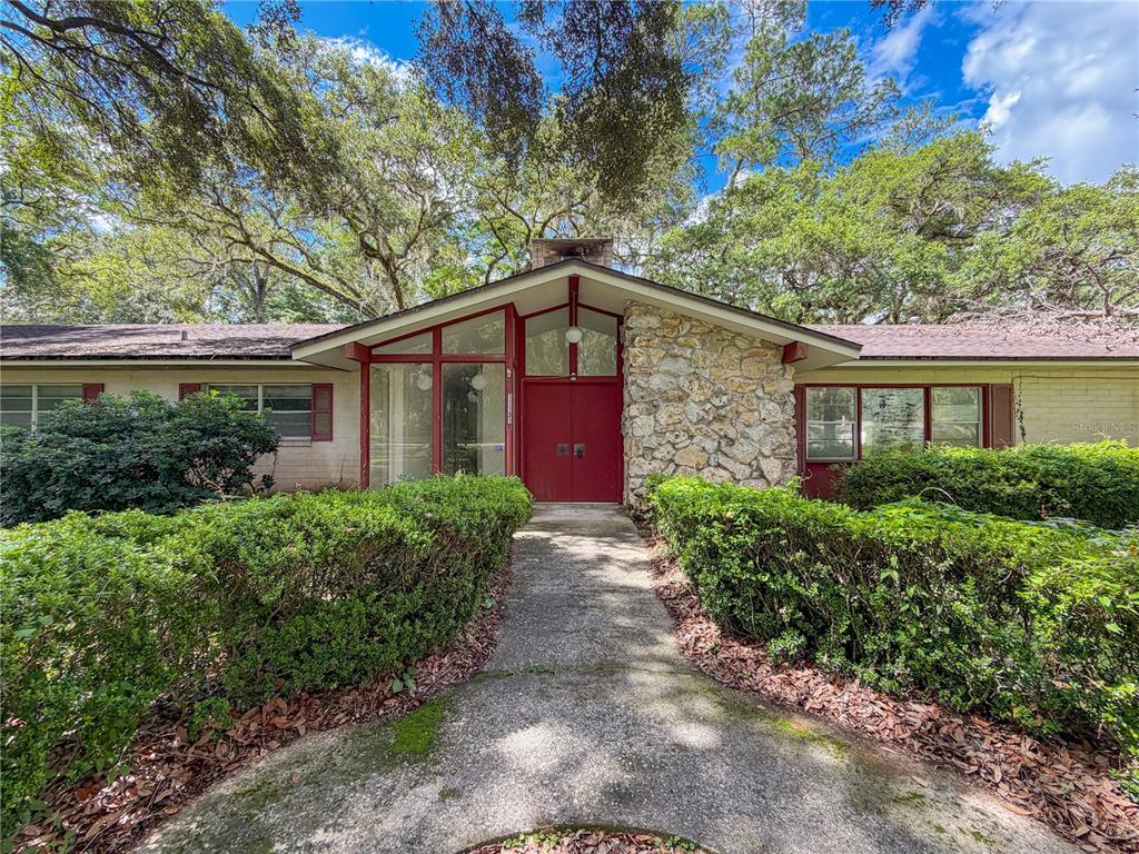 A front view of a single-story house with a stone facade and red double doors — 11131 NW 11TH AVENUE, GAINESVILLE, FL