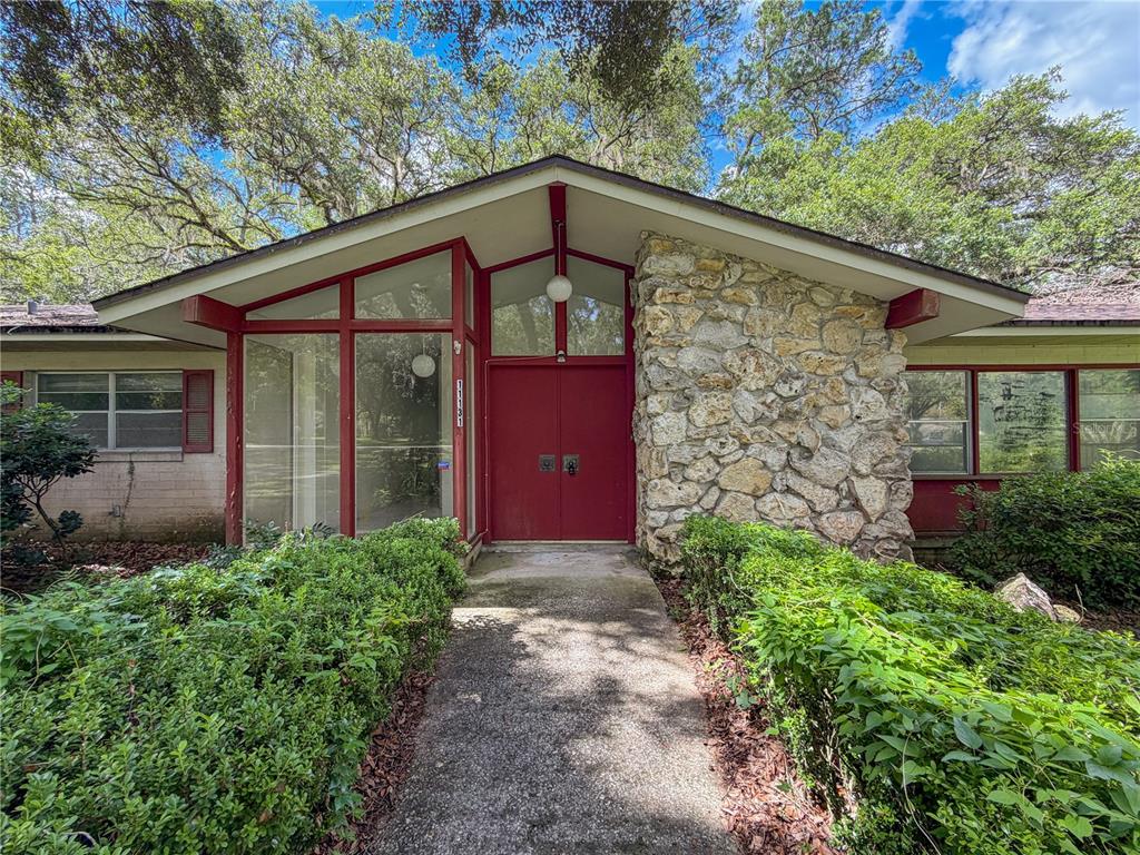 The front exterior of a mid-century modern home features a stone facade and red doors — 11131 NW 11TH AVENUE, GAINESVILLE, FL