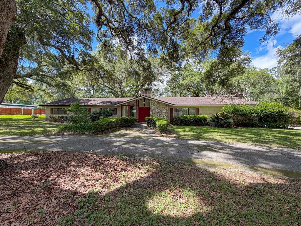 A single-story ranch-style house features a stone facade, a red front door, and a driveway — 11131 NW 11TH AVENUE, GAINESVILLE, FL