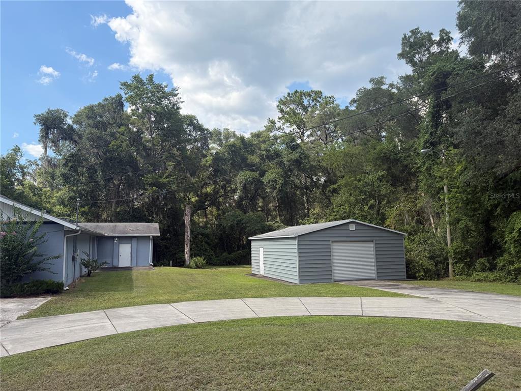 A detached metal garage sits on a grassy lot next to a blue house — 5561 NE 35TH STREET, SILVER SPRINGS, FL