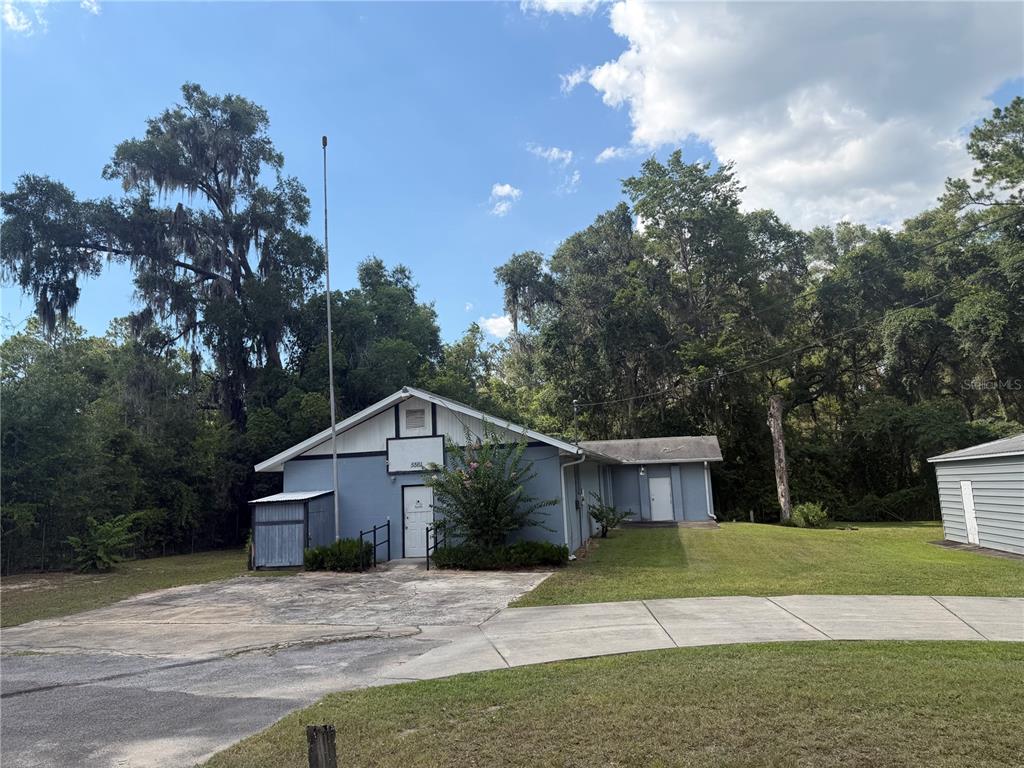 A blue, single-story building with a concrete driveway sits on a grassy, tree-lined lot — 5561 NE 35TH STREET, SILVER SPRINGS, FL