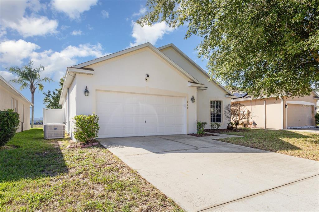 A single-story house with a white stucco exterior, a two-car garage, and a concrete driveway — 213 KNOLLWOOD DRIVE, DAVENPORT, FL