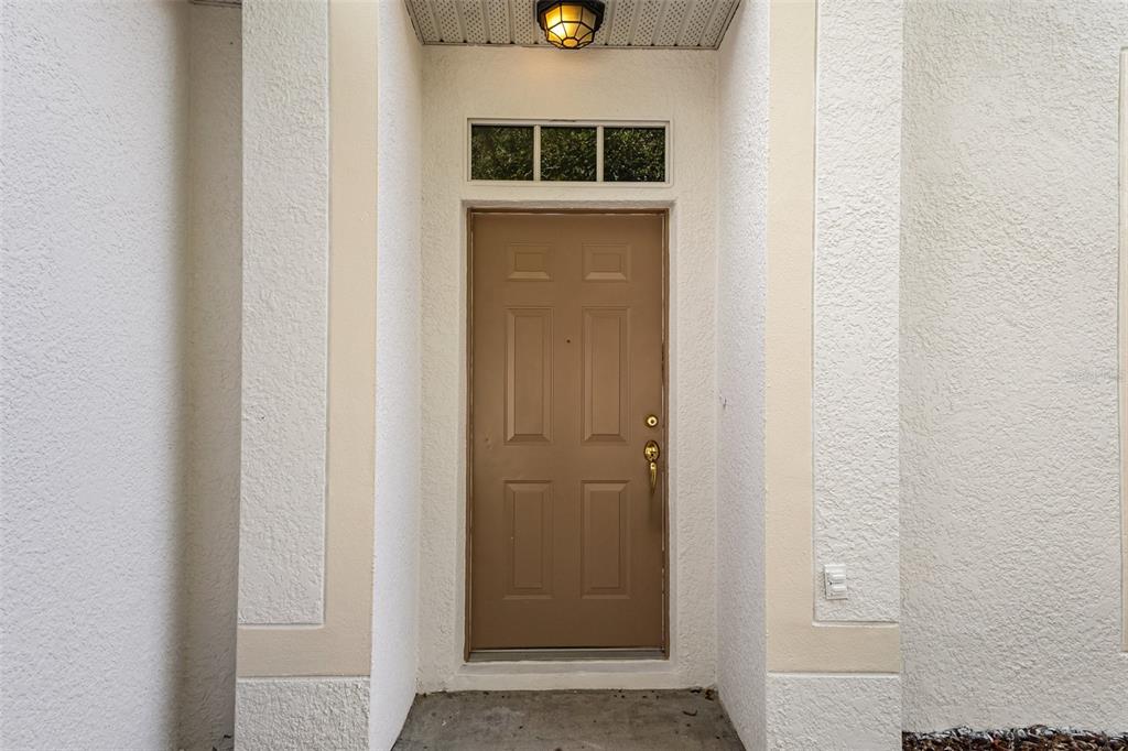 A brown six-panel front door with a transom window is set between two stucco walls — 213 KNOLLWOOD DRIVE, DAVENPORT, FL