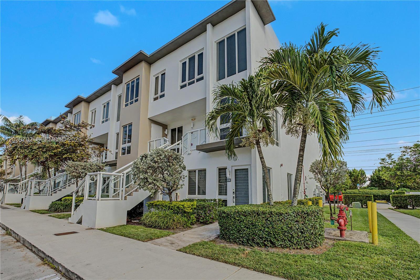 A modern three-story townhouse with white stucco walls, exterior staircases, and palm trees — 10260 NW 63 Terrace # 213, Miami FL 33178, MIAMI, FL