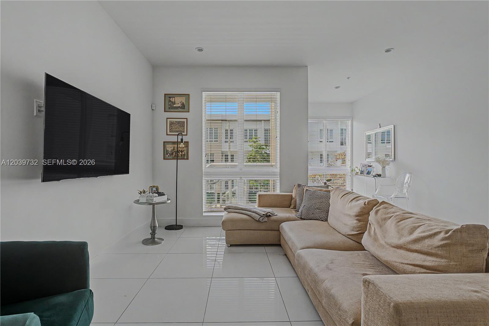 A living room features a beige sectional sofa, a wall-mounted television, and white tile flooring — 10260 NW 63 Terrace # 213, Miami FL 33178, MIAMI, FL