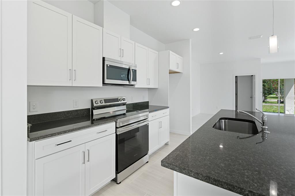 A kitchen features white cabinets, dark granite countertops, stainless steel appliances, and a center island — 817 S LOCUST AVENUE, SANFORD, FL