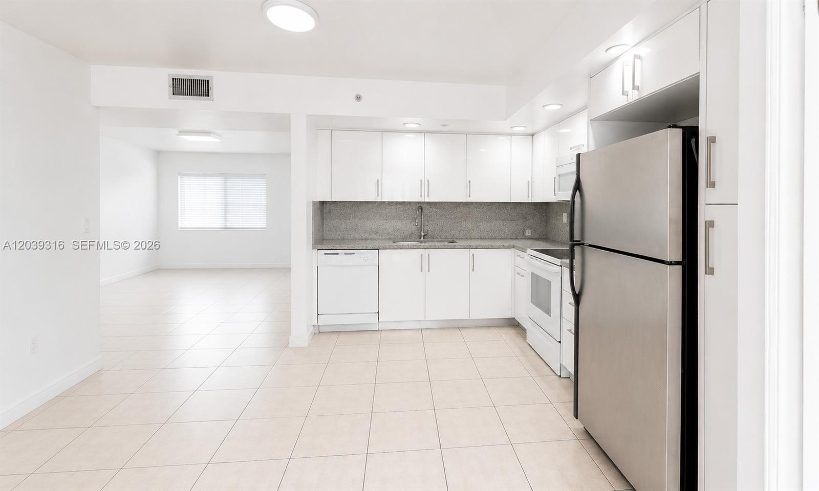 A kitchen with white cabinets, stainless steel appliances, and tile flooring opens to a room — 8700 SW 133rd Ave Rd # 312, Miami FL 33183, MIAMI, FL