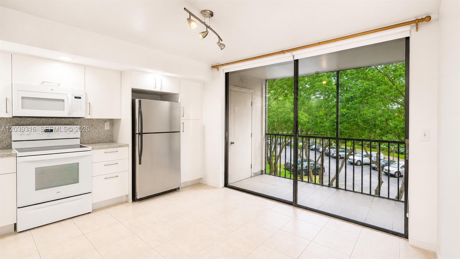 A kitchen with white cabinets and stainless steel appliances opens onto a screened balcony — 8700 SW 133rd Ave Rd # 312, Miami FL 33183, MIAMI, FL