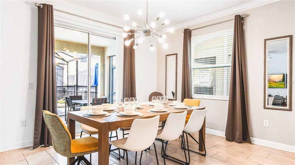 A dining room features a wooden table, mixed seating, a modern chandelier, and sliding glass doors — 2936 PROTAGONIST STREET, KISSIMMEE, FL