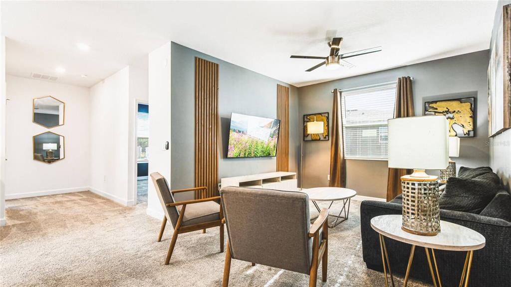 A living room features a wall-mounted television, wood slat accents, gray carpet, and modern furniture — 2936 PROTAGONIST STREET, KISSIMMEE, FL