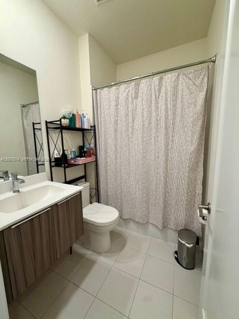 A bathroom features a wood-toned vanity, a toilet, and a shower with a patterned curtain — DORAL, FL