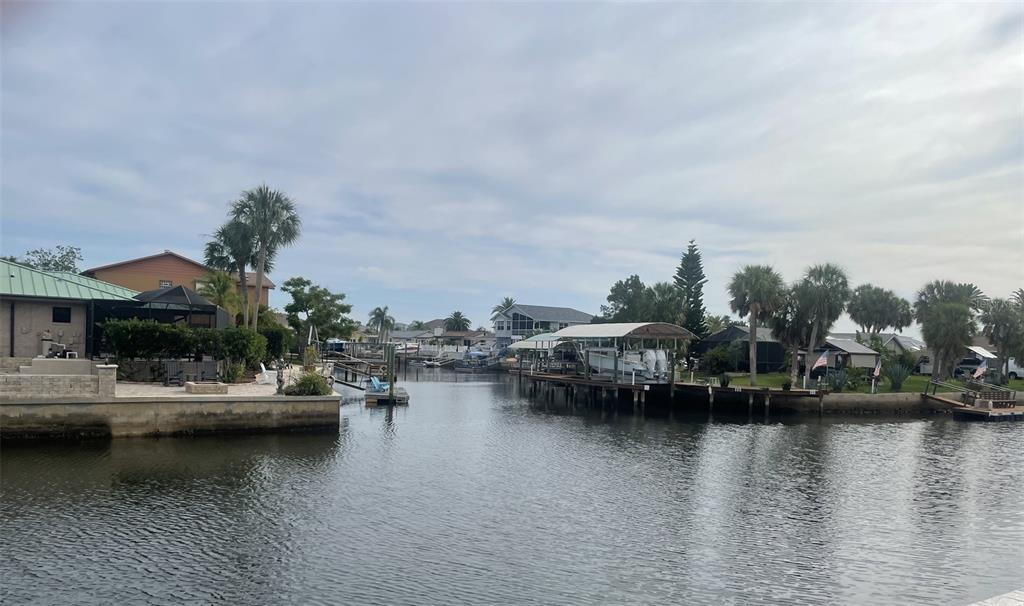A canal view featuring waterfront homes, boat docks, and palm trees under a cloudy sky — 7128 SOUTHWIND DRIVE, HUDSON, FL