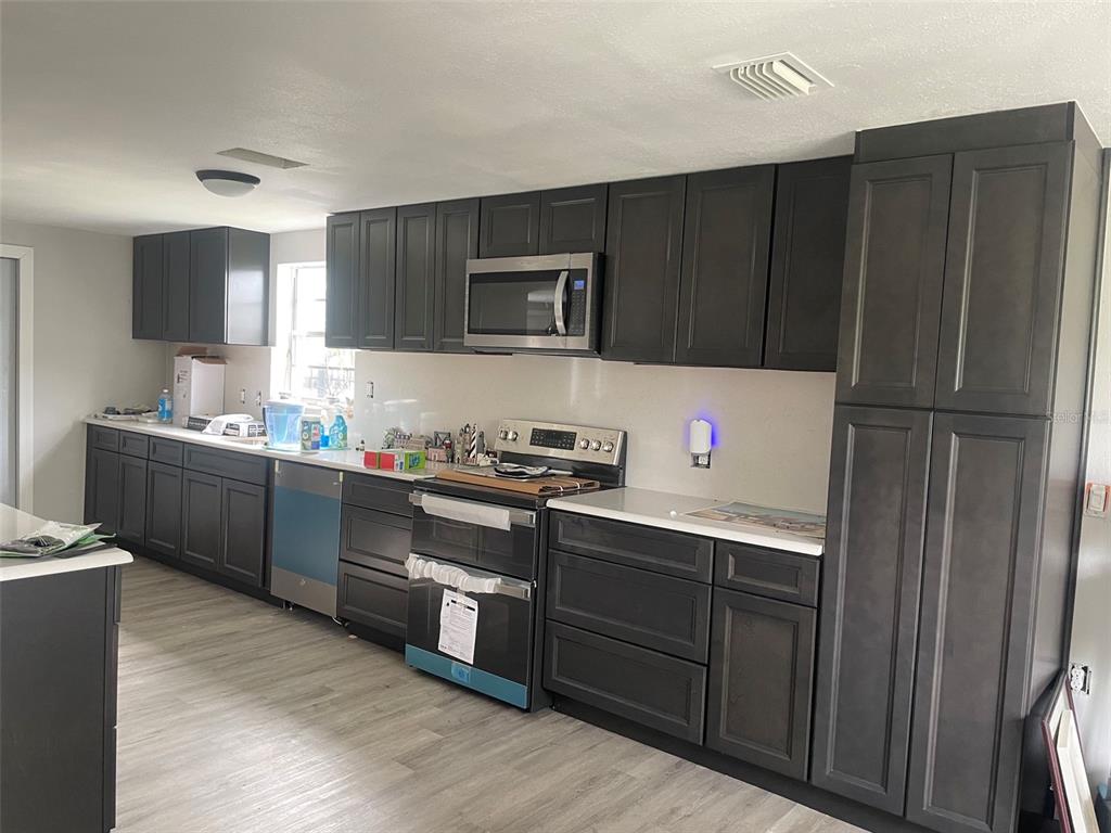 A kitchen features dark cabinetry, a white quartz island, and stainless steel appliances — 7128 SOUTHWIND DRIVE, HUDSON, FL