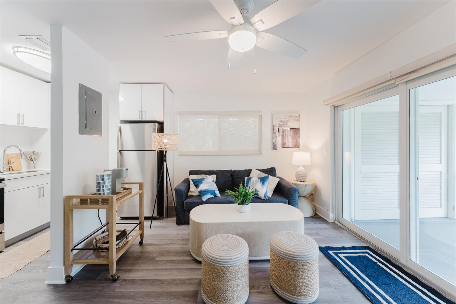 A living room with a blue sofa, coffee table, two ottomans, and an adjacent kitchen — 501 N Ocean Boulevard, Boca Raton FL 33432, BOCA RATON, FL
