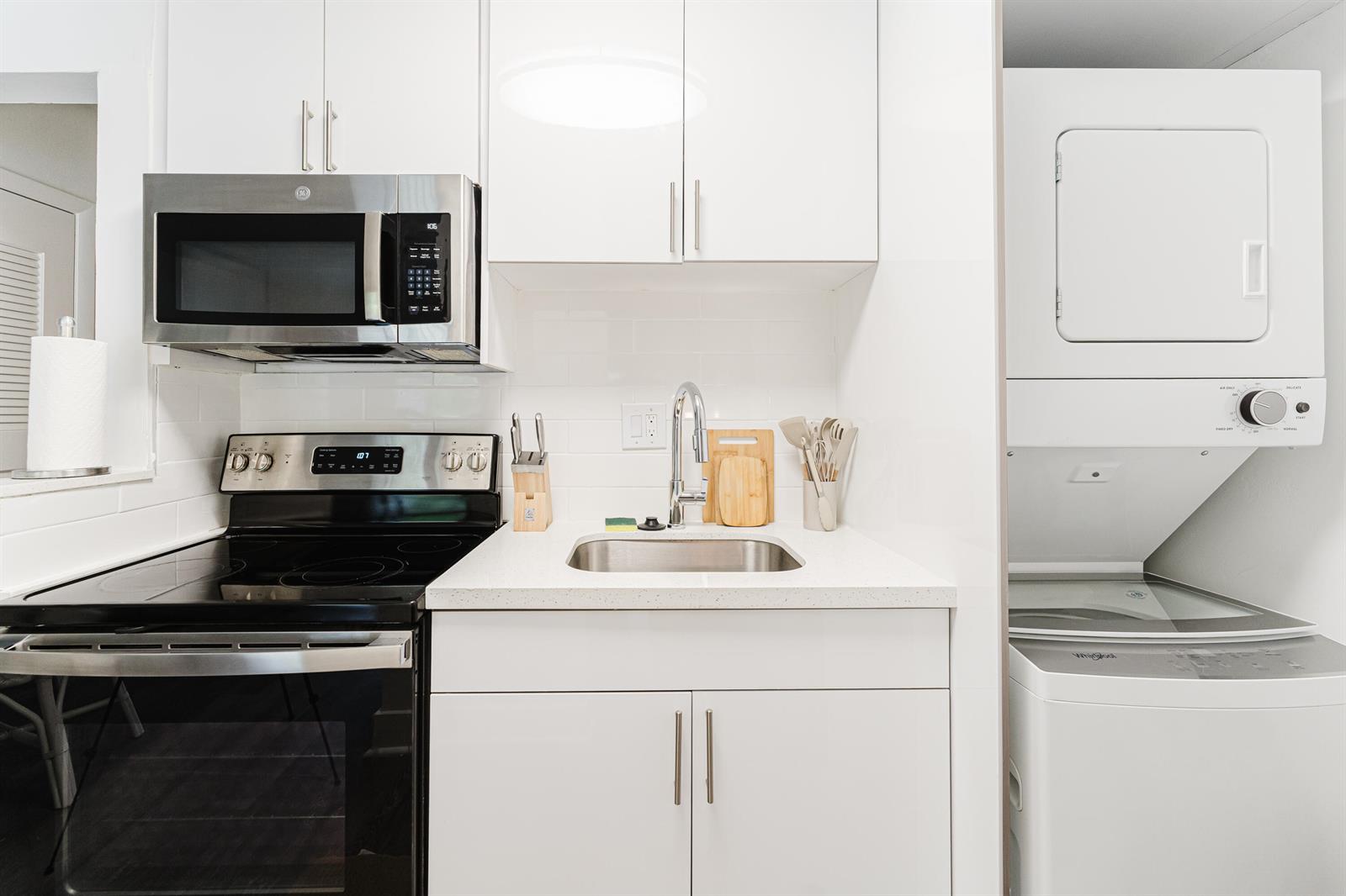 A compact kitchen features white cabinets, stainless steel appliances, a small sink, and laundry units — 501 N Ocean Boulevard, Boca Raton FL 33432, BOCA RATON, FL