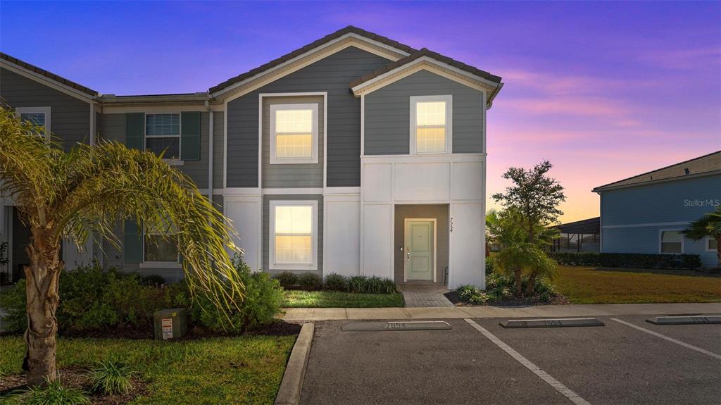 A two-story townhouse exterior features gray siding, white trim, and a paved parking area — 7554 OAK SPRING LANE, DAVENPORT, FL