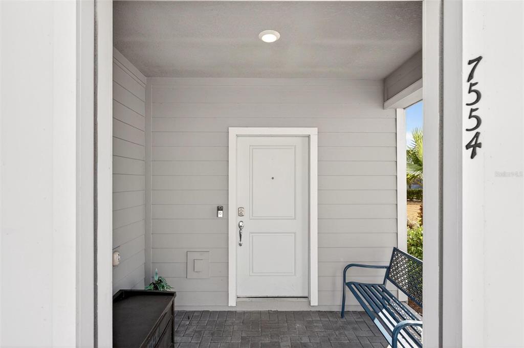 A covered entryway features gray horizontal siding, a white door, and a blue metal bench — 7554 OAK SPRING LANE, DAVENPORT, FL