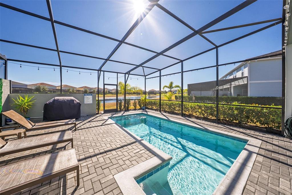 A screened-in patio features a rectangular swimming pool, lounge chairs, and a covered grill — 7554 OAK SPRING LANE, DAVENPORT, FL