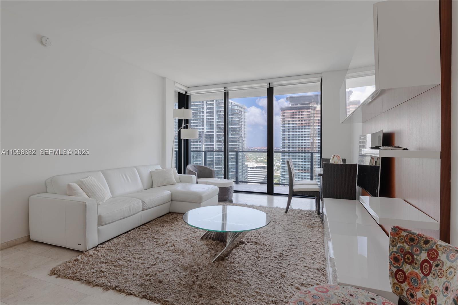 A modern living room features a white sectional sofa, glass coffee table, and floor-to-ceiling windows — 68 SE 6th St # 3006, Miami FL 33131, MIAMI, FL