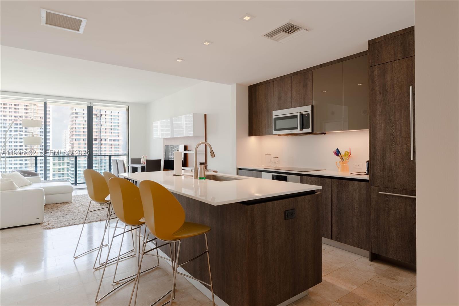A modern kitchen features dark wood cabinetry, a white island with bar seating, and floor-to-ceiling windows — 68 SE 6th St # 3006, Miami FL 33131, MIAMI, FL
