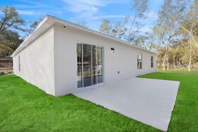 The exterior of a white house features a concrete patio and a sliding glass door — 3216 E ANDERSON STREET, INVERNESS, FL