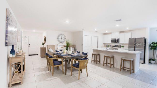 An open-concept kitchen and dining area features white cabinets, stainless steel appliances, and tile flooring — 3216 E ANDERSON STREET, INVERNESS, FL
