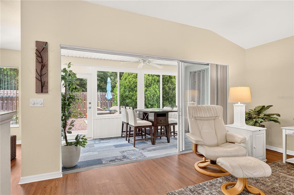 A living room with wood-look flooring, a plaid armchair, a floor lamp, and an entryway door — 13088 SE 86TH CIRCLE, SUMMERFIELD, FL