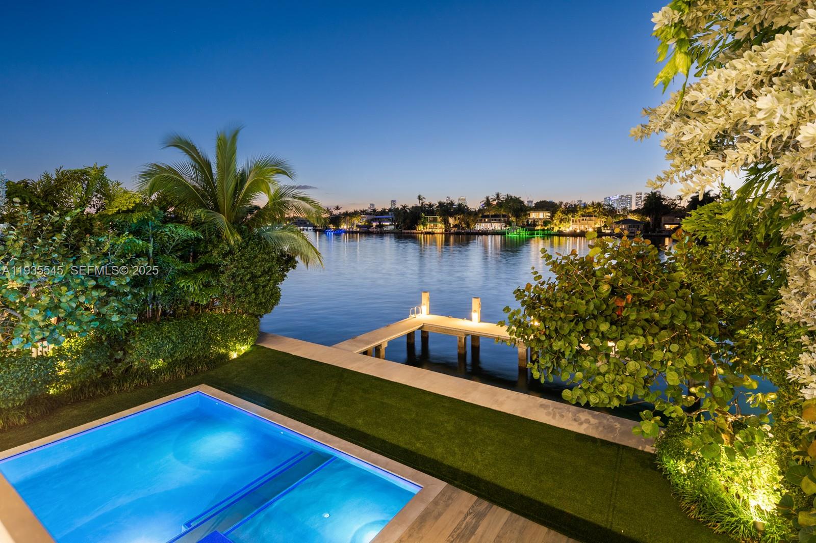 An illuminated swimming pool and private dock overlook a waterfront view at twilight — 40 W Rivo Alto Dr, Miami Beach FL 33139, MIAMI BEACH, FL