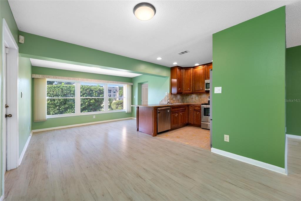 An open-concept kitchen with wood cabinets and stainless steel appliances overlooks a light-floored living area — 8440 BRENTWOOD ROAD, SEMINOLE, FL