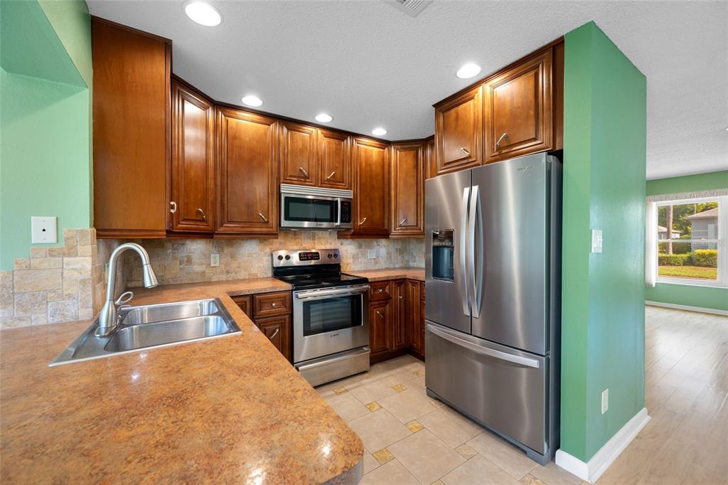 A kitchen features wood cabinets, stainless steel appliances, a stone backsplash, and a laminate countertop — 8440 BRENTWOOD ROAD, SEMINOLE, FL