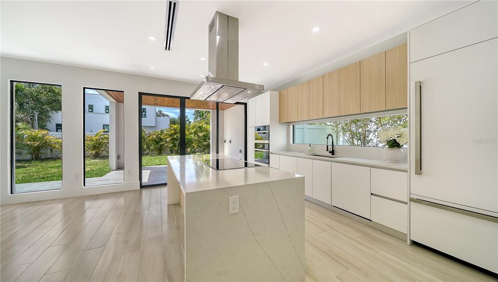 A modern kitchen features a large quartz island, light wood cabinets, and floor-to-ceiling windows — 1734 WISCONSIN LANE, SARASOTA, FL