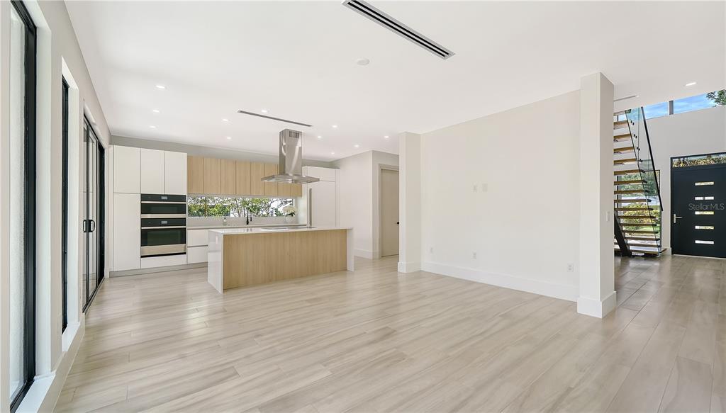 A modern kitchen and living area feature light wood flooring, white cabinetry, and a staircase — 1734 WISCONSIN LANE, SARASOTA, FL