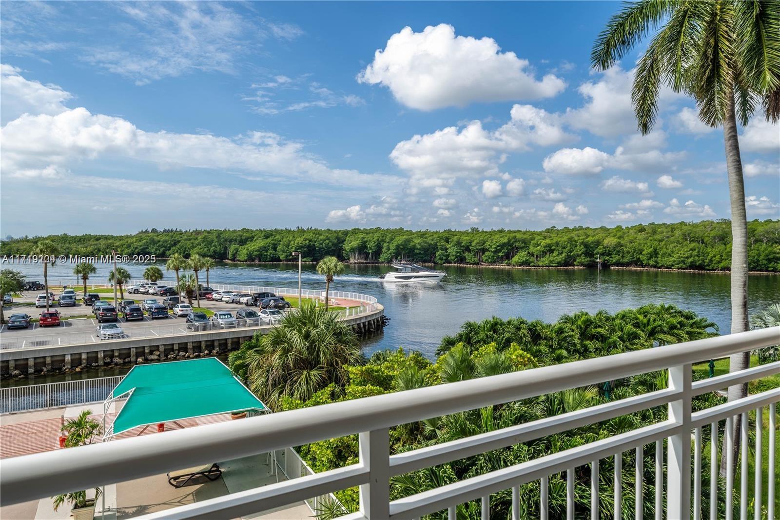 A balcony overlooks a parking lot, a waterway with a boat, and lush green trees — SUNNY ISLES BEACH, FL