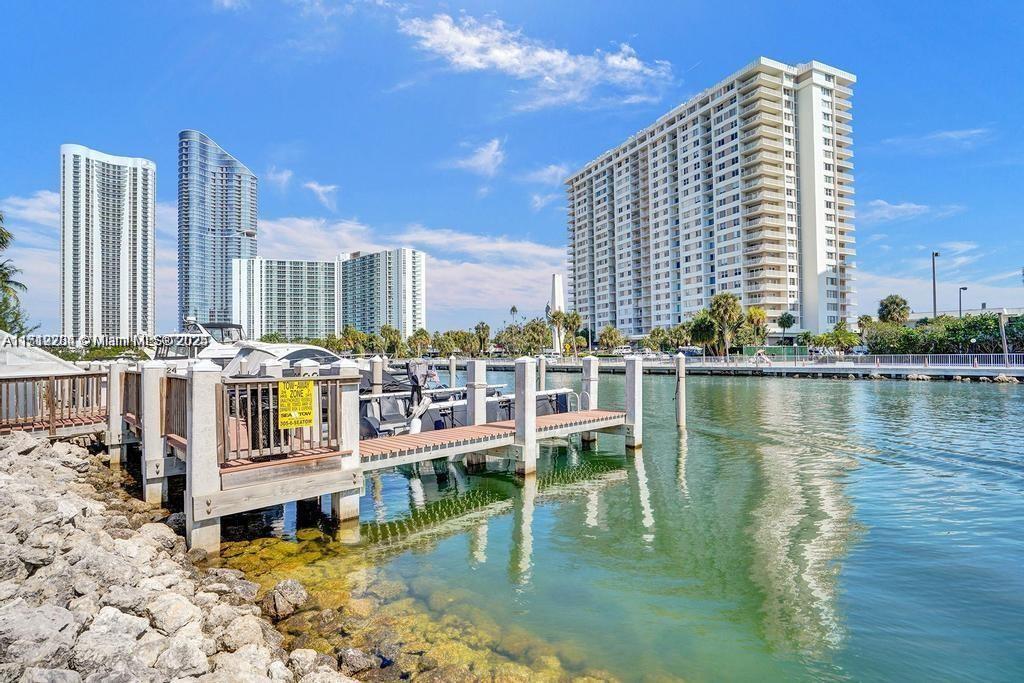 A wooden boat dock extends into a canal with high-rise apartment buildings in the background — SUNNY ISLES BEACH, FL
