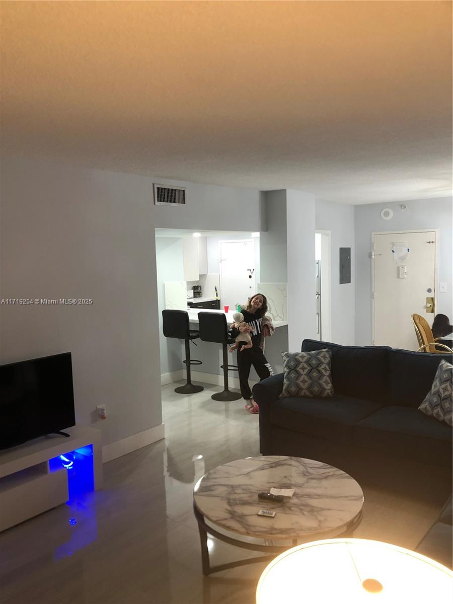 A living room with a marble coffee table, dark sofa, and an open kitchen area — SUNNY ISLES BEACH, FL