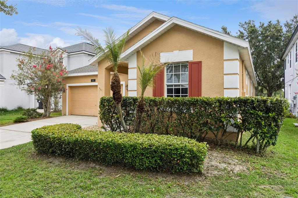 A tan single-story house features a garage, a front hedge, and red window shutters — 4627 BLUE MAJOR DRIVE, WINDERMERE, FL