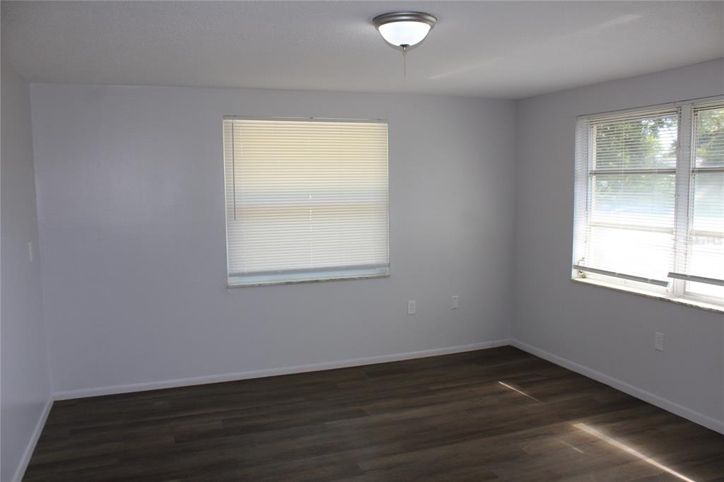 An empty room features light gray walls, dark wood-look flooring, and two windows with blinds — 322 ORGAN STREET UNIT A & B, PUNTA GORDA, FL