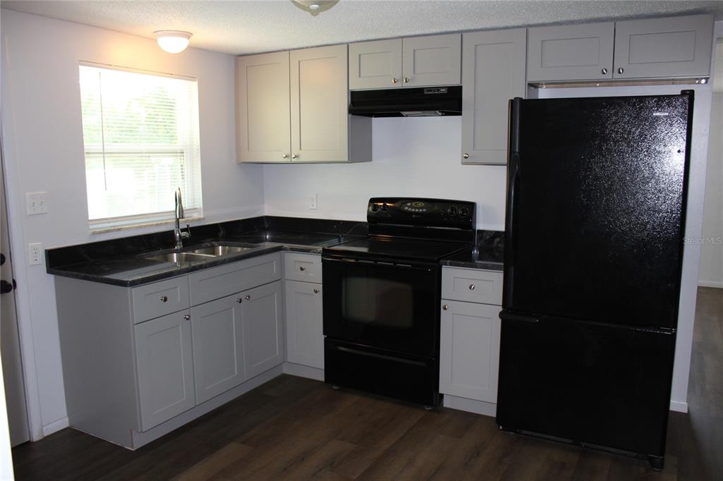 A kitchen features gray cabinets, black countertops, black appliances, and wood-look flooring — 322 ORGAN STREET UNIT A & B, PUNTA GORDA, FL