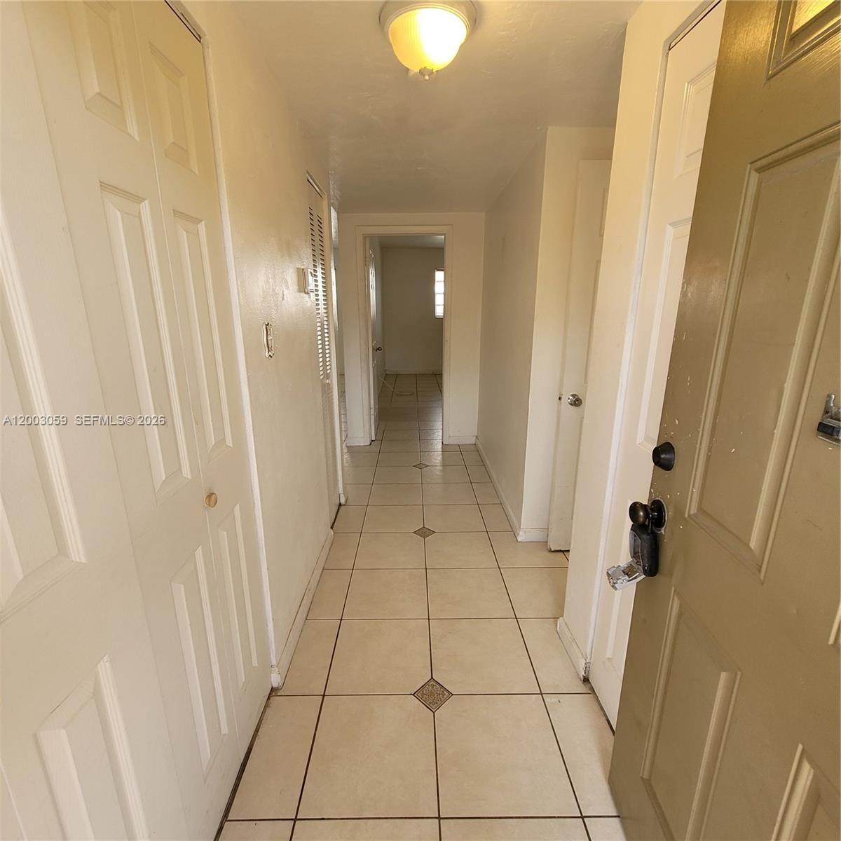 A hallway with beige tile flooring leads to a doorway in a residential interior — 1370 NE 119th St # 137015, Miami FL 33161, MIAMI, FL