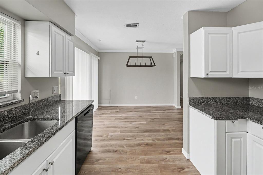 A kitchen with white cabinets and granite countertops opens into a dining area with wood flooring — 4101 BLUEFISH DRIVE SE, ST PETERSBURG, FL