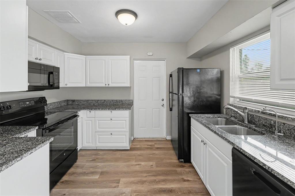 A kitchen features white cabinets, granite countertops, black appliances, and wood-look flooring — 4101 BLUEFISH DRIVE SE, ST PETERSBURG, FL