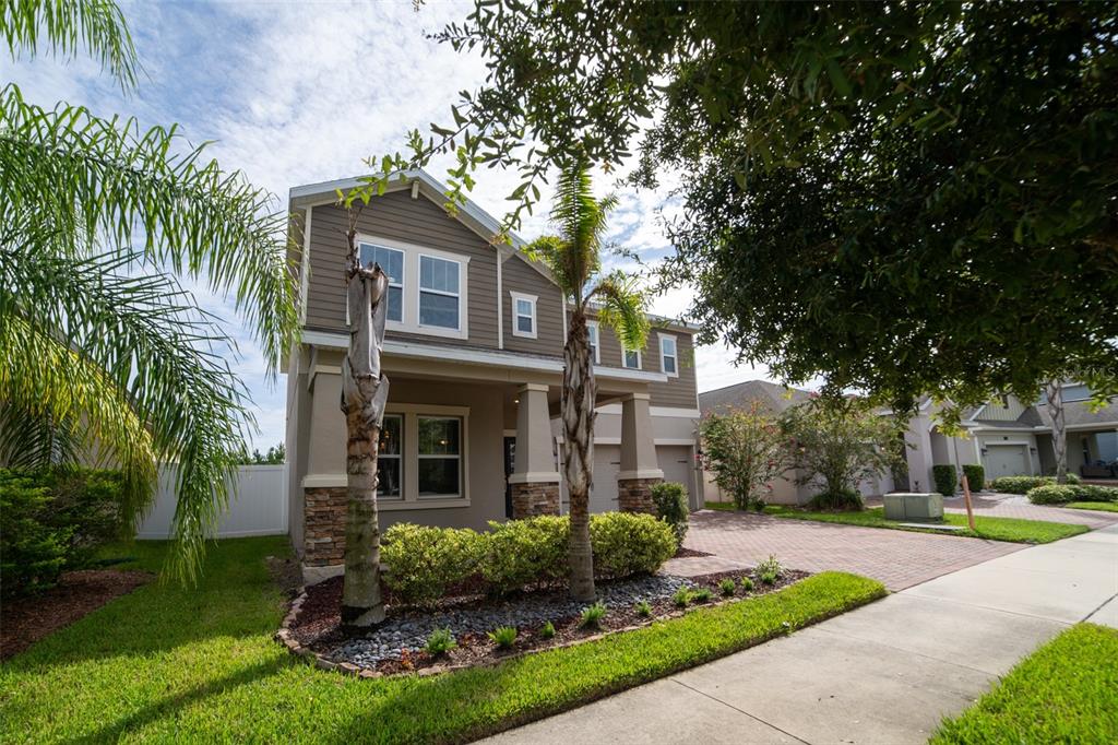 A two-story house with a brick driveway, stone accents, and palm trees in the front yard — 11109 SWEETGUM WOODS DRIVE, ORLANDO, FL