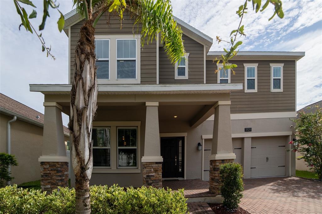 A two-story house with tan siding, stone accents on the porch columns, and a garage — 11109 SWEETGUM WOODS DRIVE, ORLANDO, FL