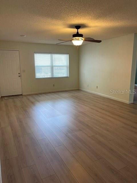 An empty room features light wood-look flooring, a ceiling fan, and a white entry door — 8540 SW 91ST PLACE UNIT C, OCALA, FL